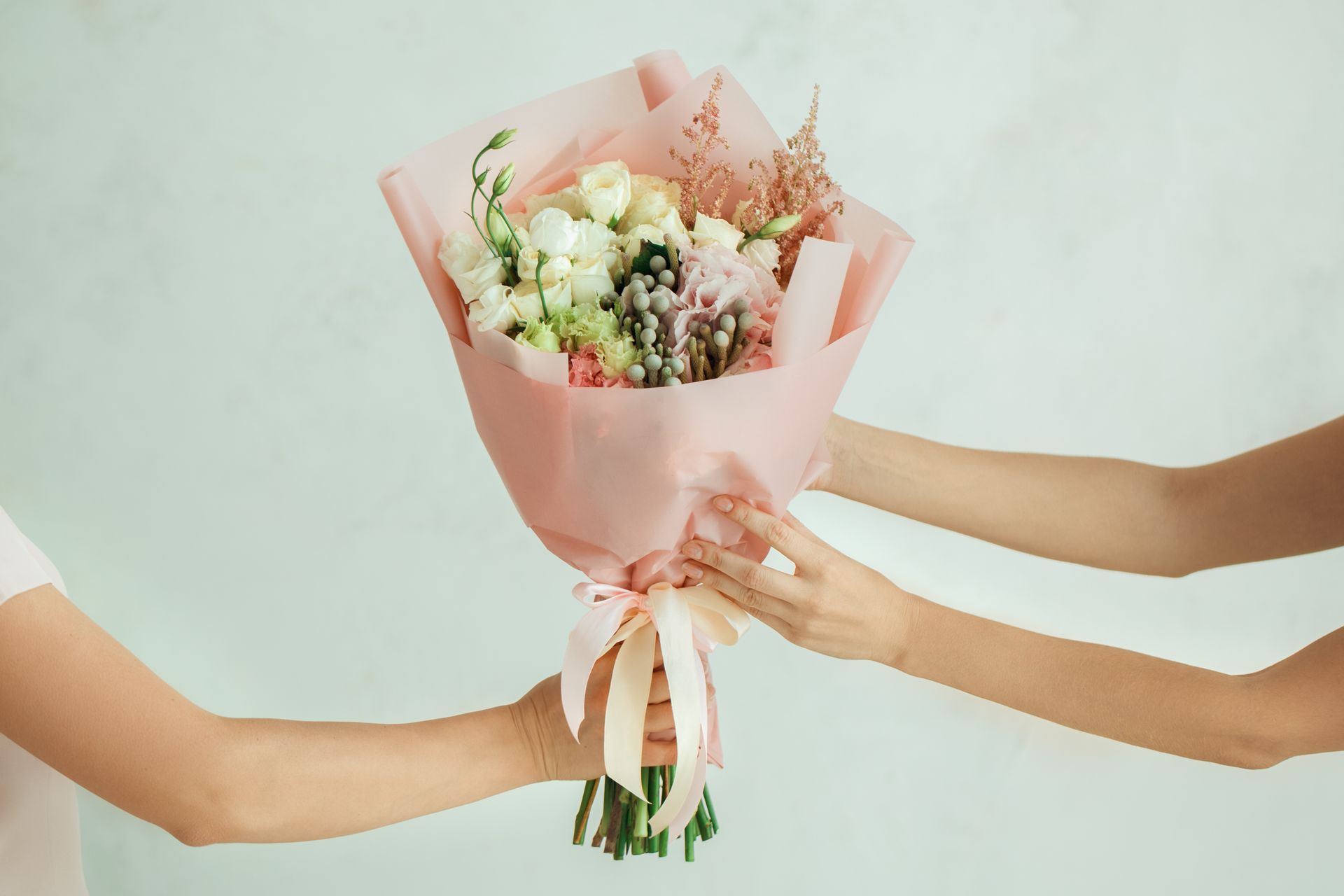 Deux mains échangent un bouquet de fleurs mélangées enveloppé de rose.