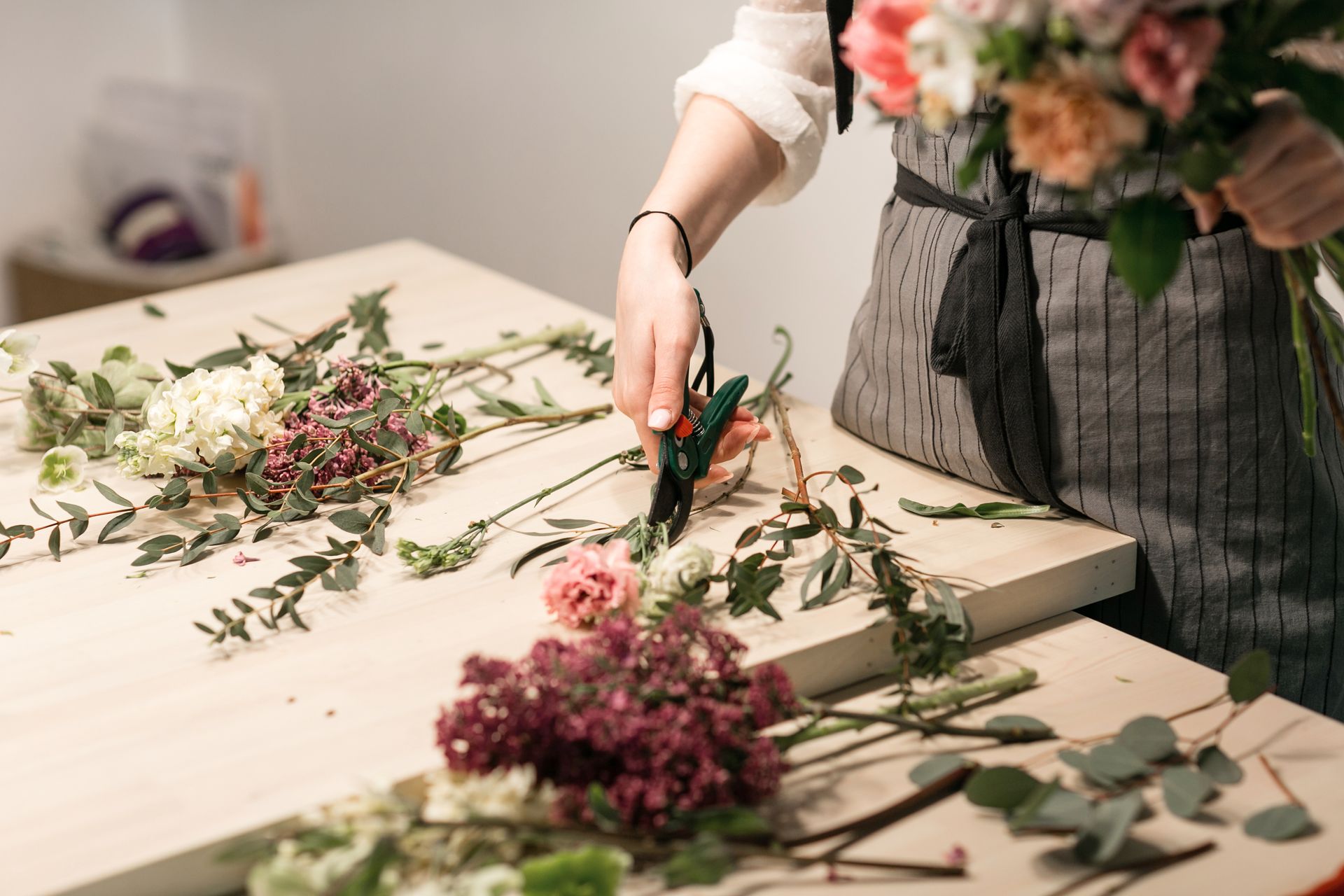 Une personne dispose des fleurs sur une table, avec des tiges vertes et des fleurs roses.