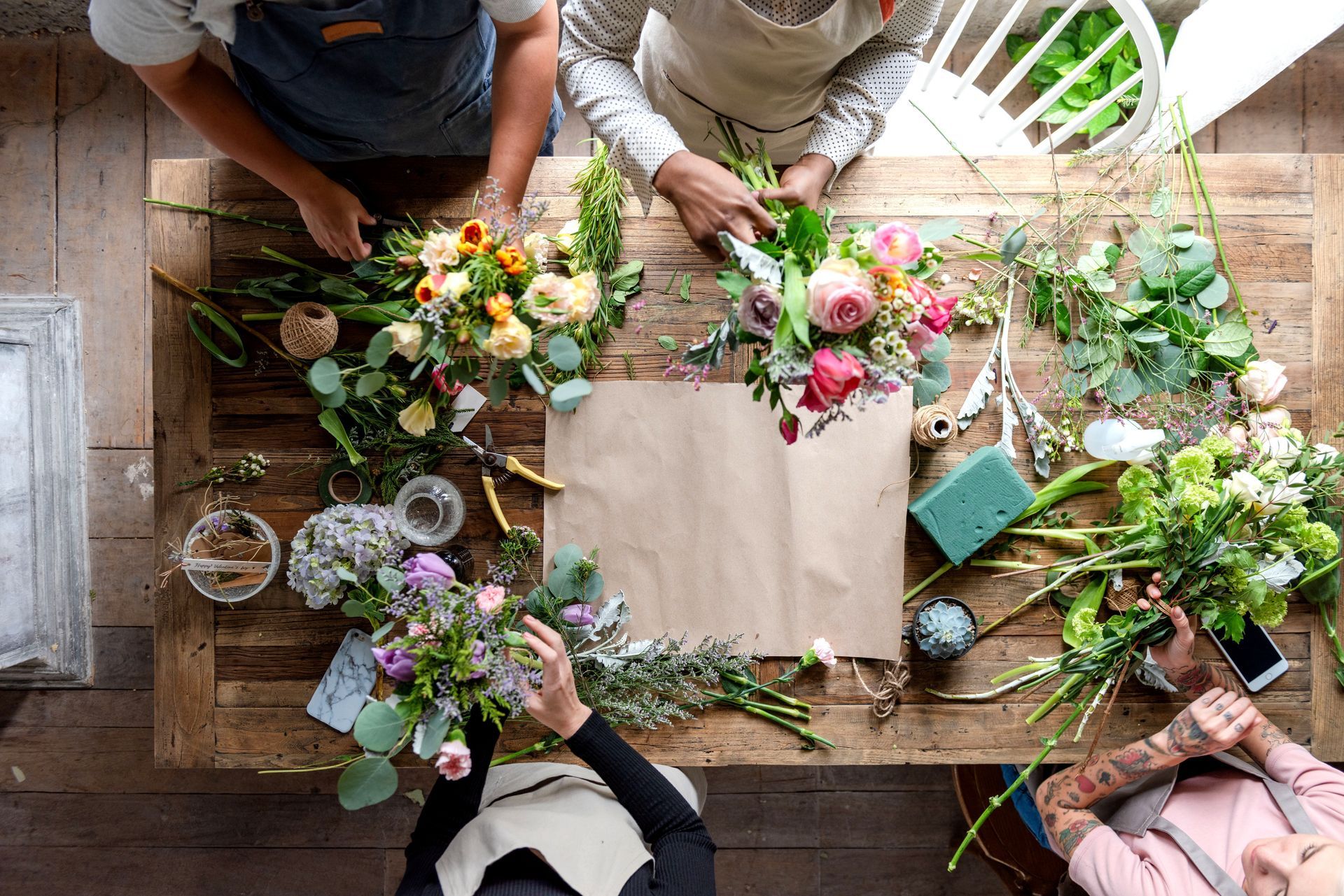 Des personnes disposent des fleurs colorées autour d'une table en bois dans un studio lumineux.