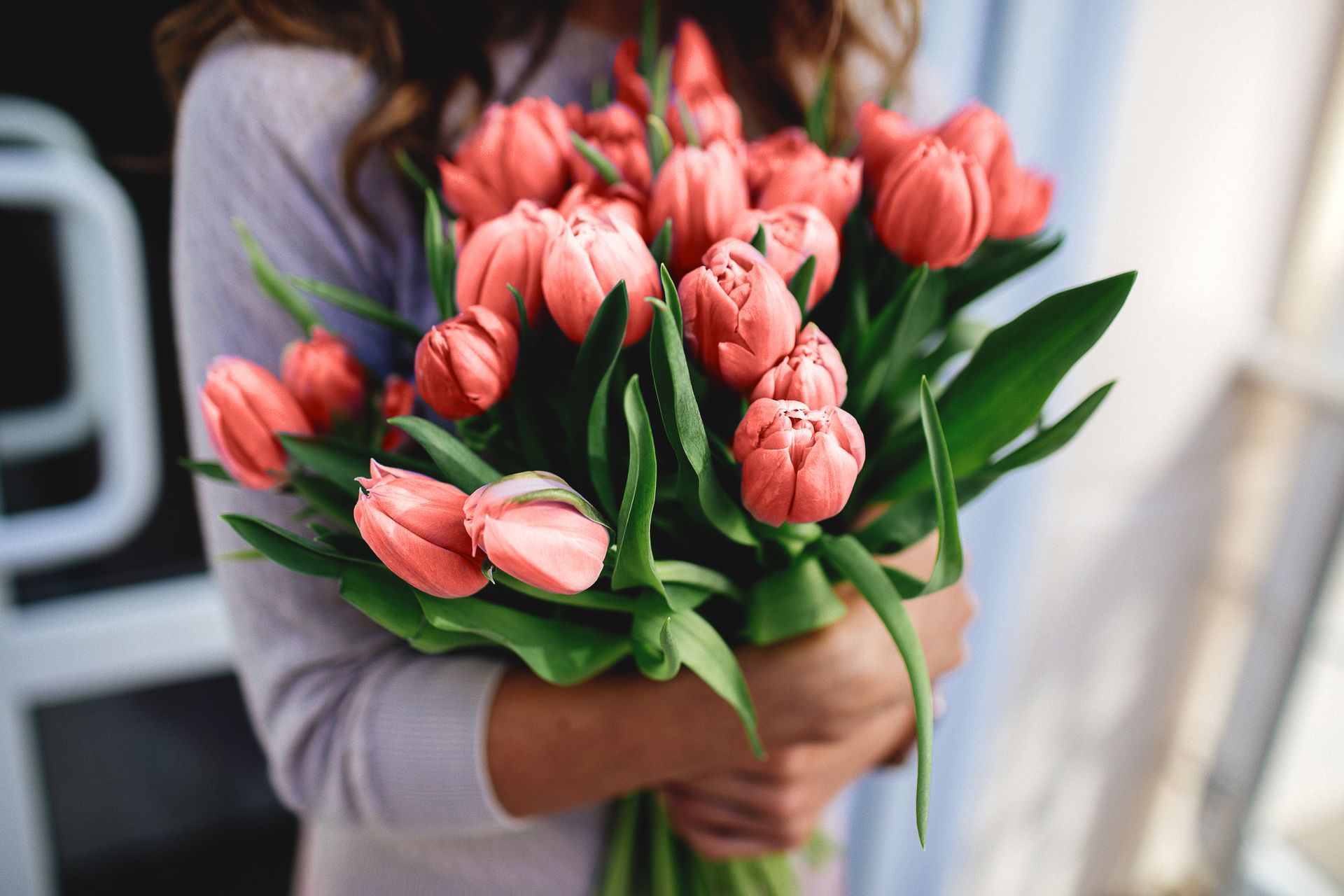 Une personne tenant un bouquet de tulipes roses à feuilles vertes à l'intérieur.