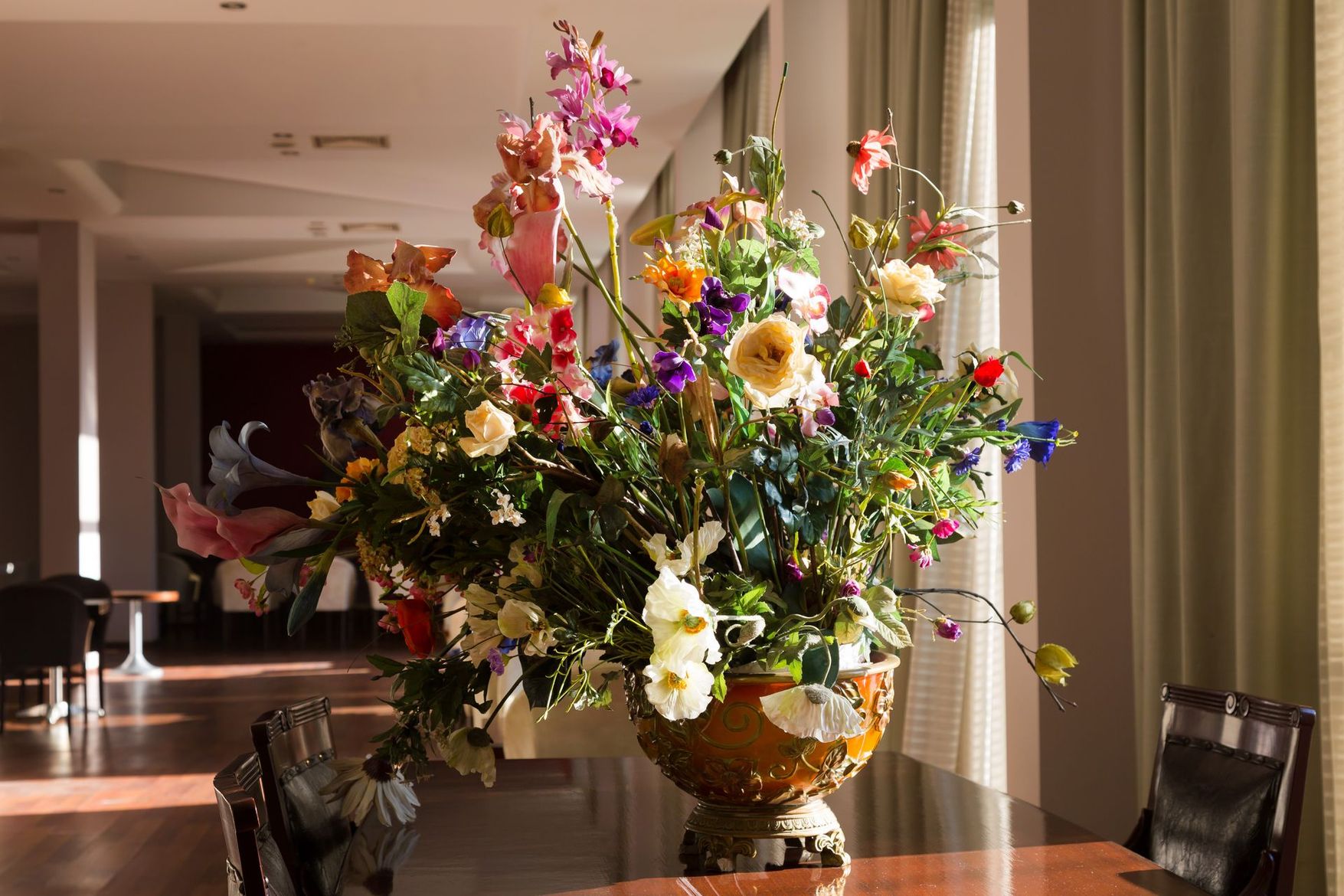 Grand arrangement floral coloré dans un vase sur une table cirée dans un couloir lumineux.