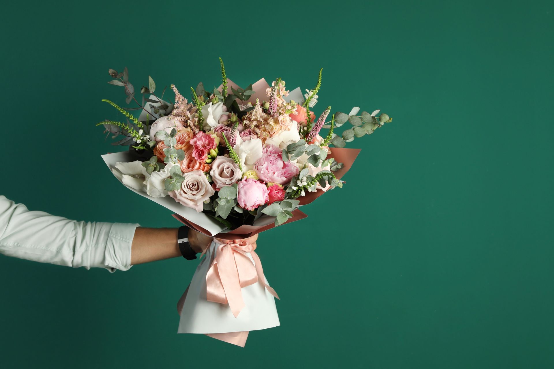 Une main tient un bouquet de fleurs rose pastel et blanches sur fond vert.