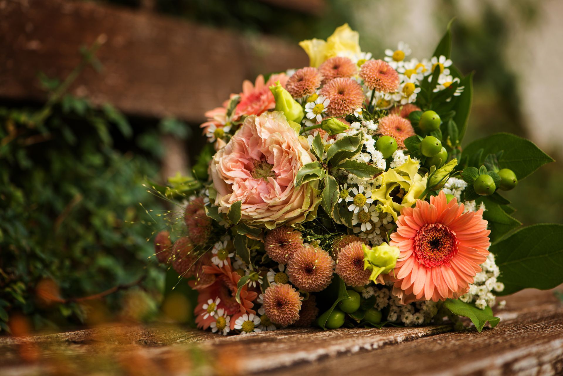 Bouquet mixte de fleurs roses, oranges et jaunes sur un banc en bois dans un jardin