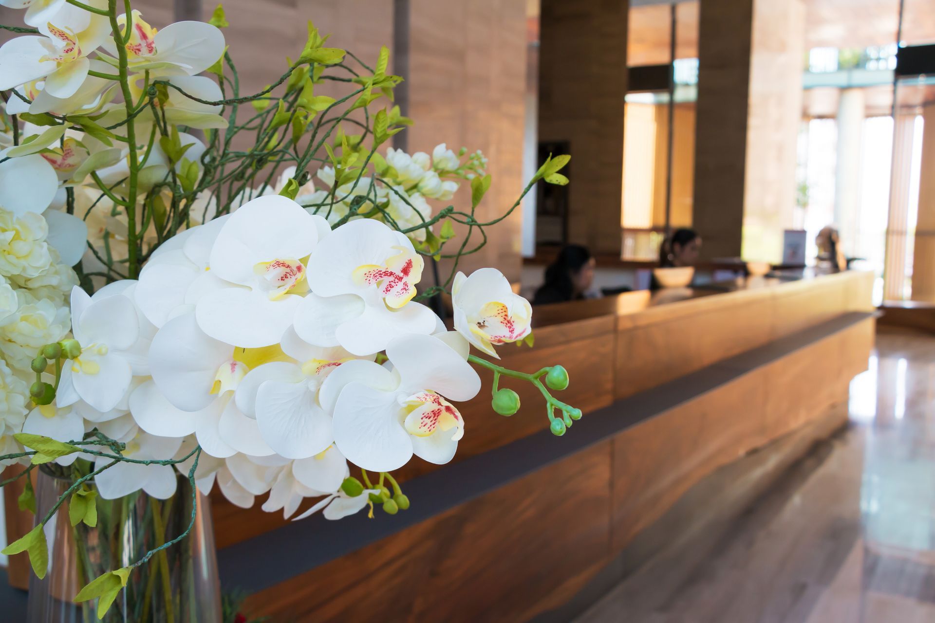 Des orchidées blanches ornent le comptoir de la réception d'un hôtel dans un hall lumineux.