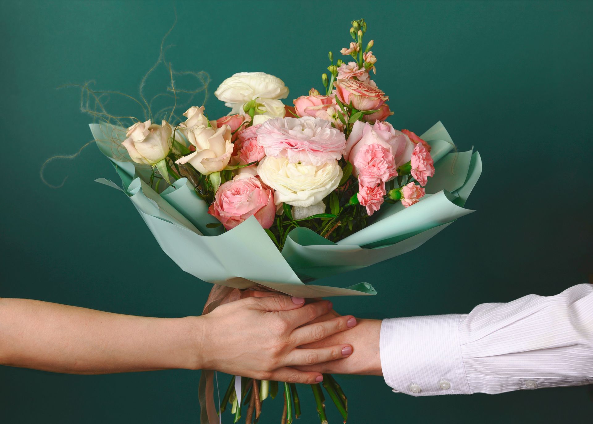 Deux mains échangeant un bouquet de fleurs roses et blanches sur fond vert.