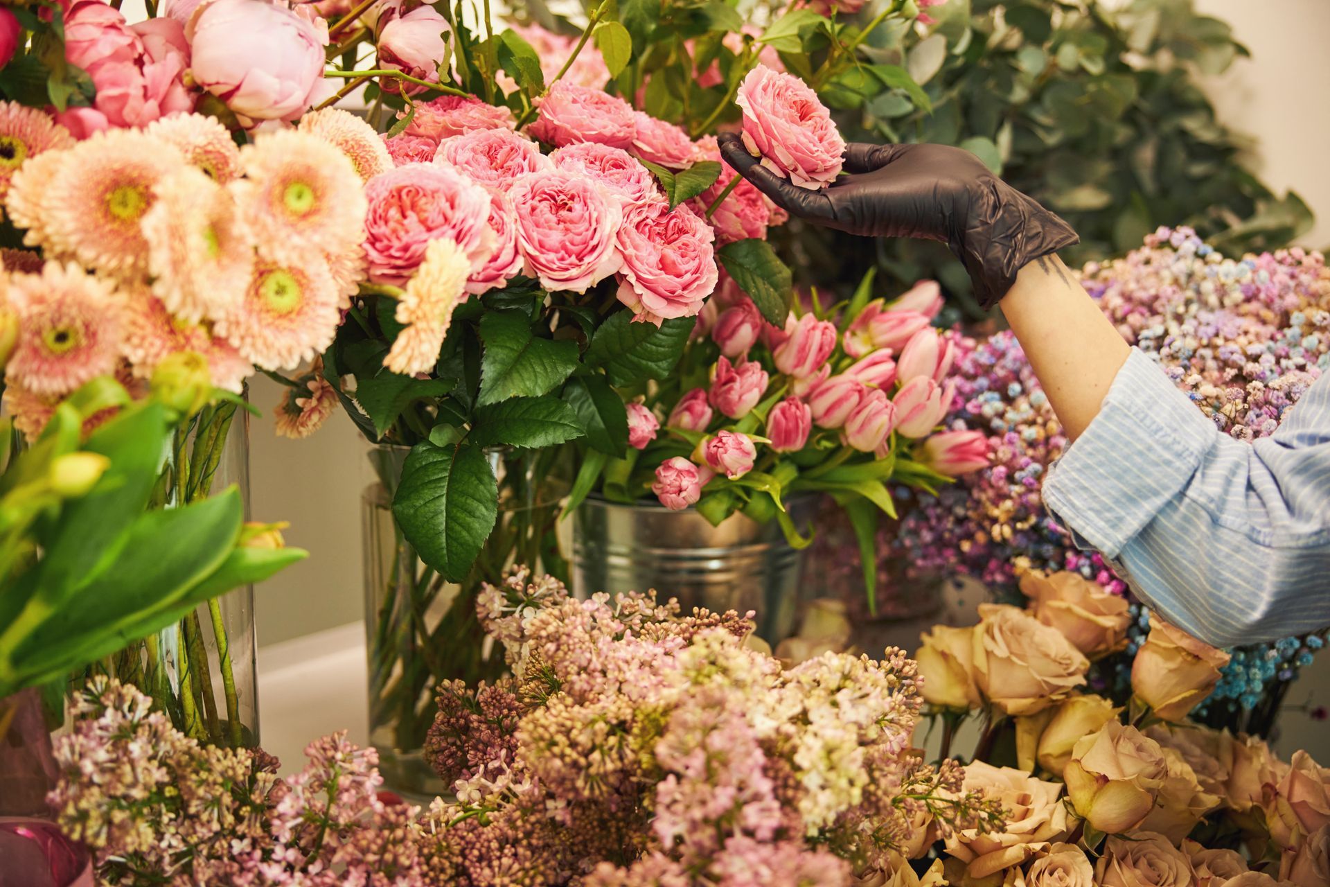 Fleuriste arrangeant des fleurs roses et crème dans une boutique de fleurs colorée.