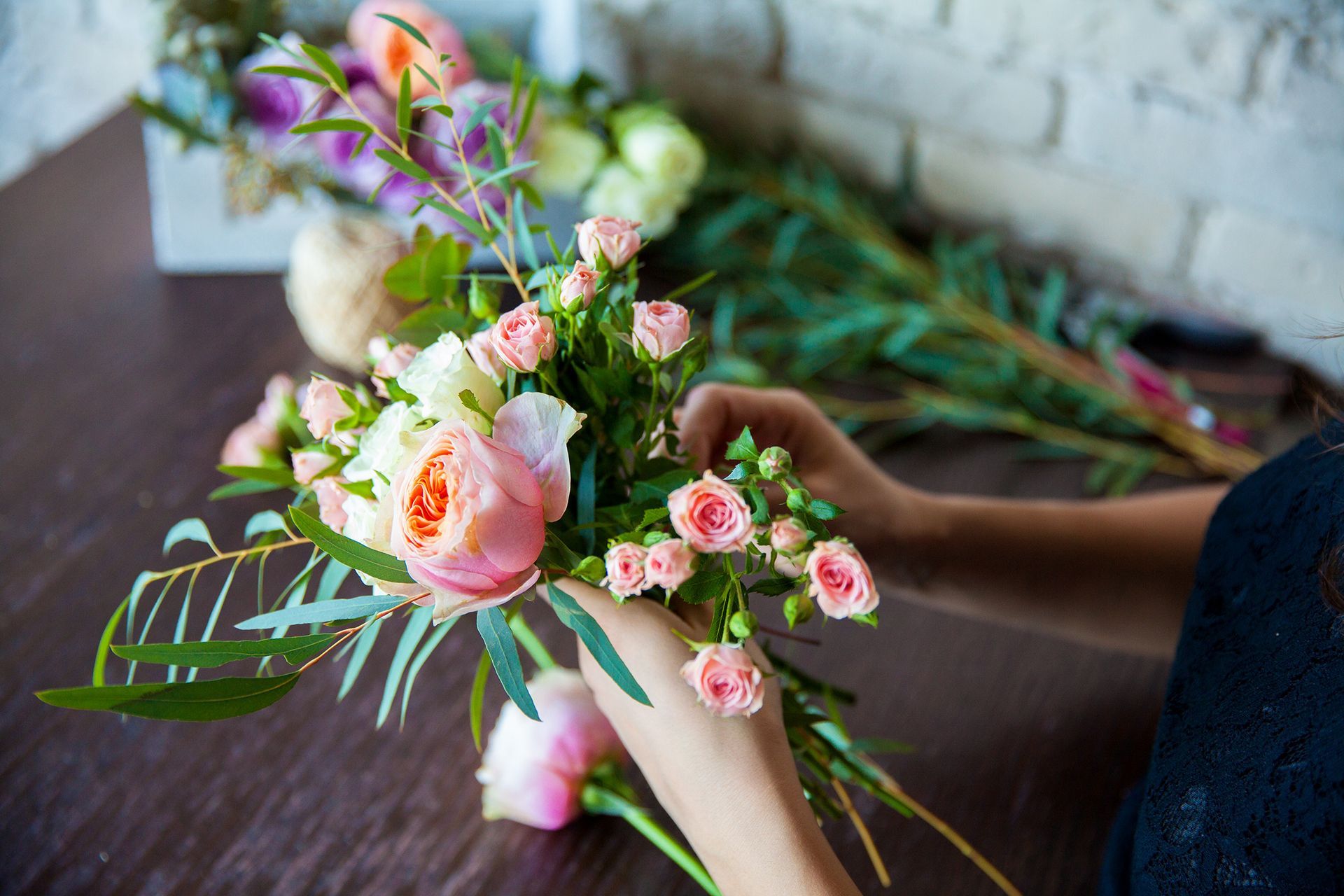Une main tenant un petit bouquet de fleurs roses et vertes, composé de verdure et de fleurs, posé sur une table en bois.