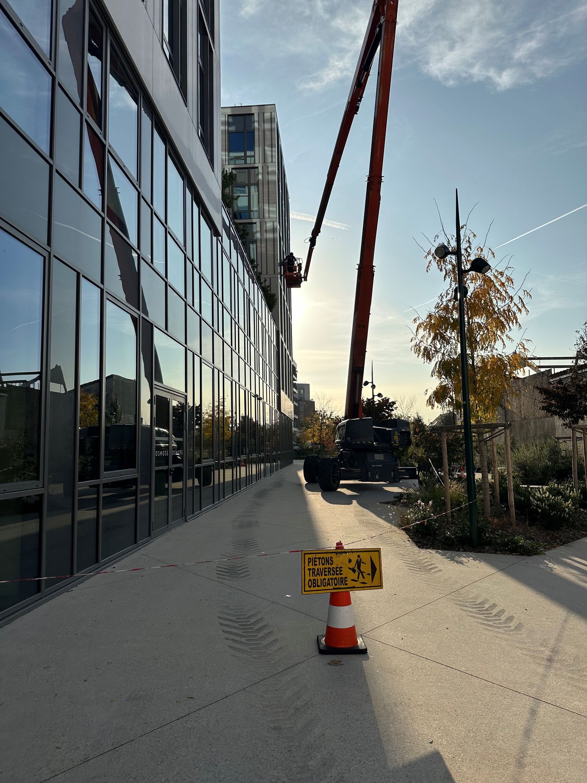 Une pompe à béton s'étend vers un bâtiment moderne. Un panneau sur un cône avertit les piétons.