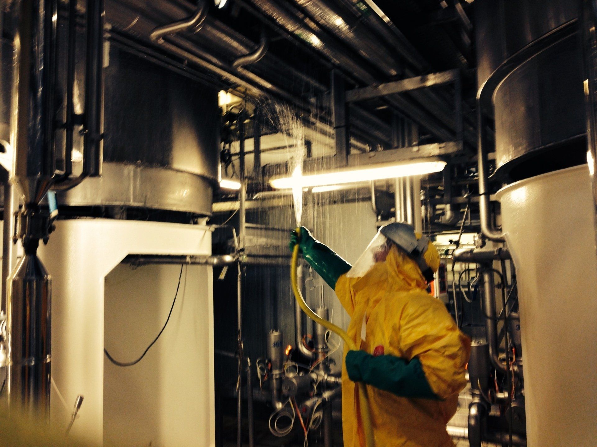 Personne en combinaison de protection jaune manipulant un équipement de pulvérisation dans un environnement industriel.