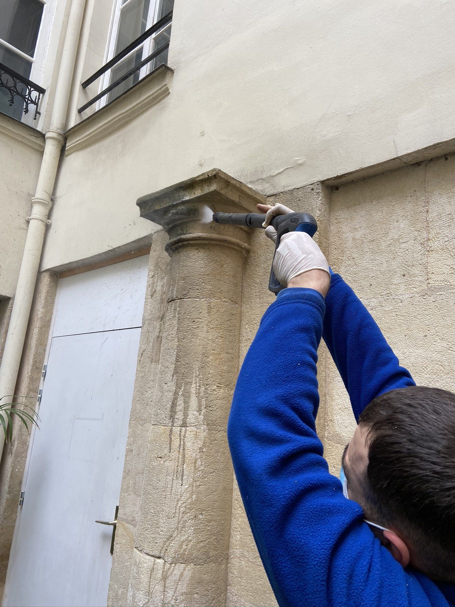 Une personne nettoie une colonne de pierre à l'extérieur avec un nettoyeur haute pression.