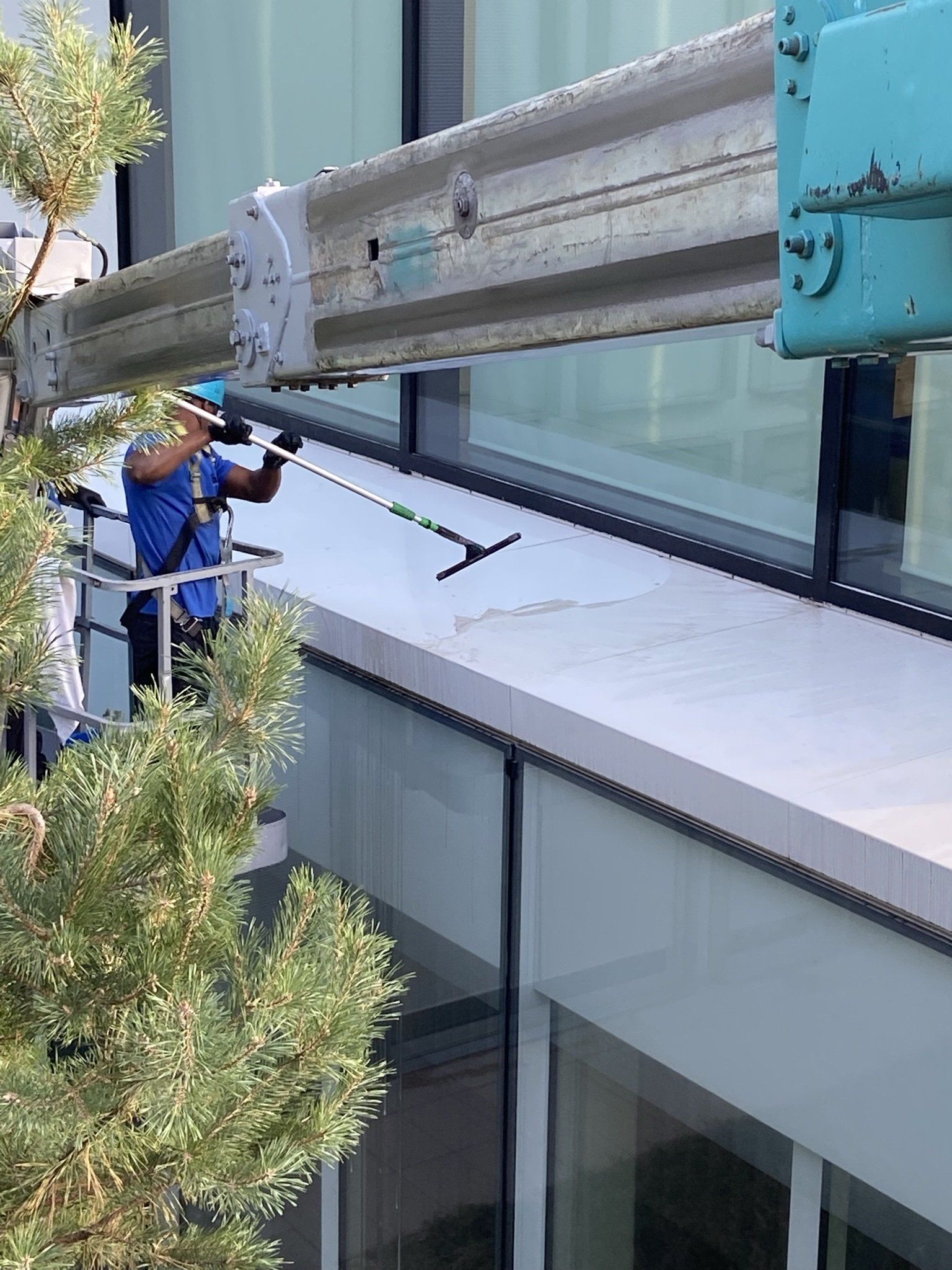 Un laveur de vitres, juché sur une nacelle, nettoie les vitres d'un immeuble de grande hauteur à l'aide d'une raclette.