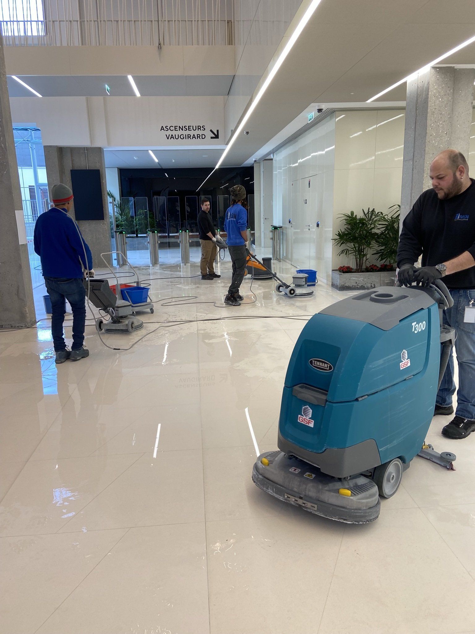 Des hommes nettoient le sol blanc brillant d'un hall d'entrée à l'aide de machines de nettoyage.