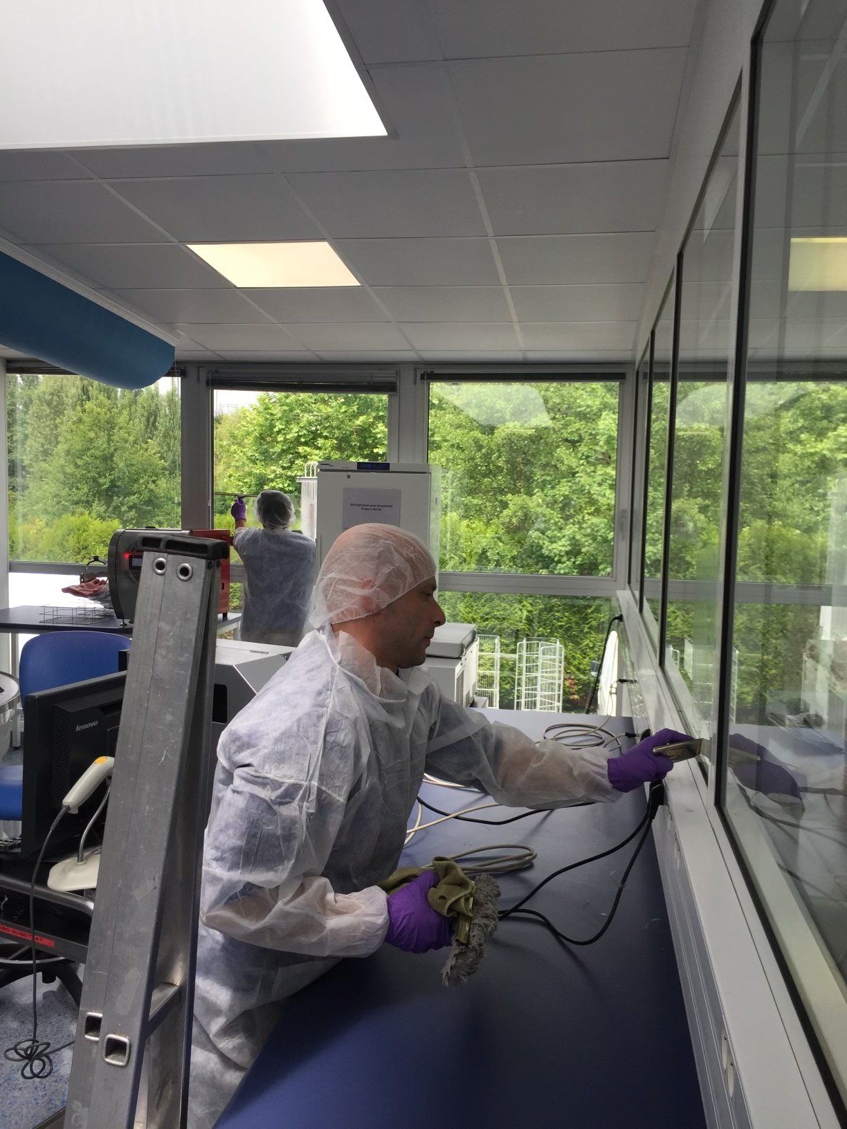 Un homme en combinaison de protection nettoie une vitre dans un laboratoire.