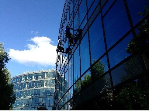 Laveurs de vitres sur un immeuble de grande hauteur aux vitres réfléchissantes ; journée ensoleillée, ciel bleu.