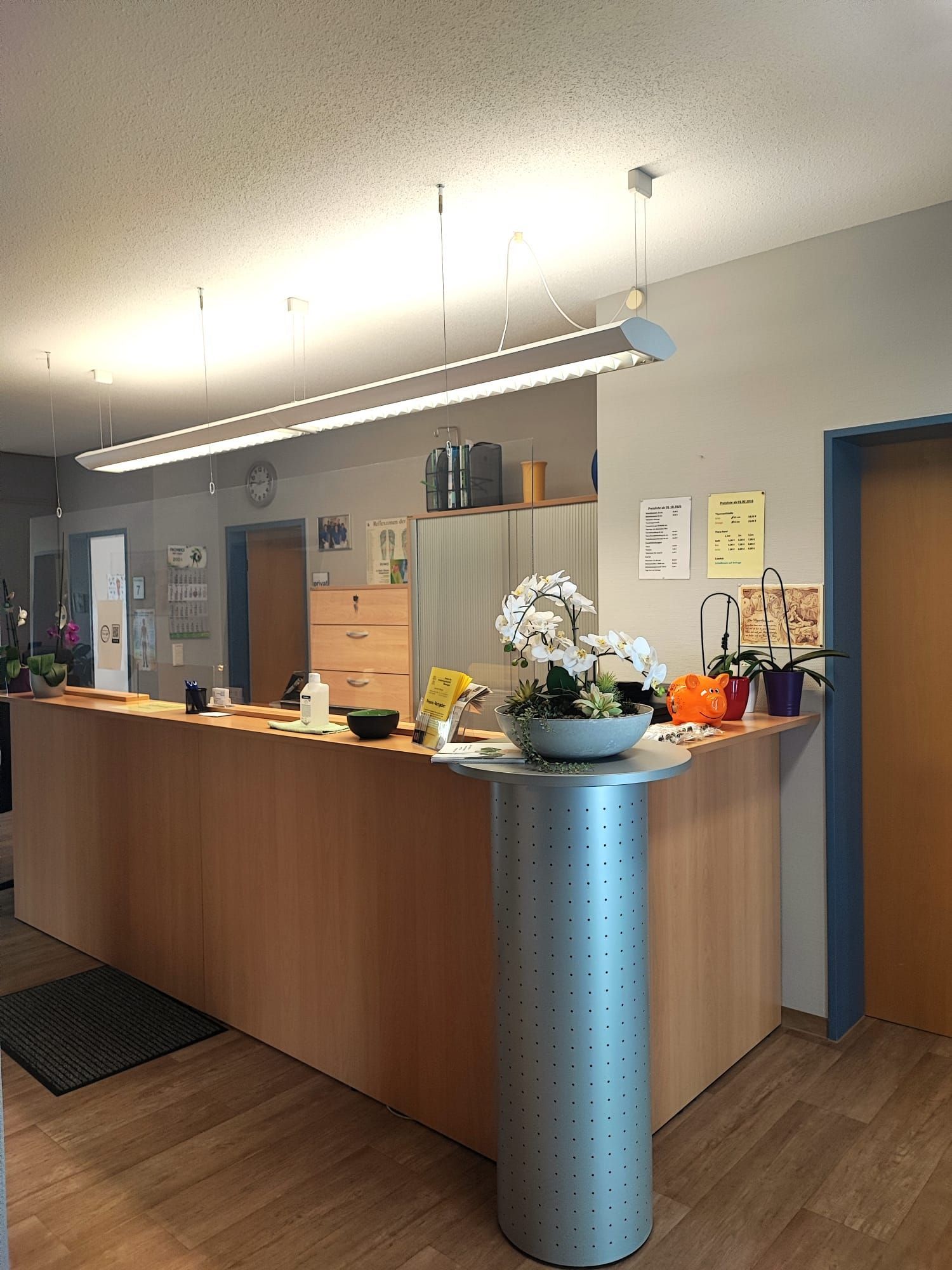 Empfangstresen in einem Büro mit heller Holztheke und grauem zylindrischem Blumenständer.