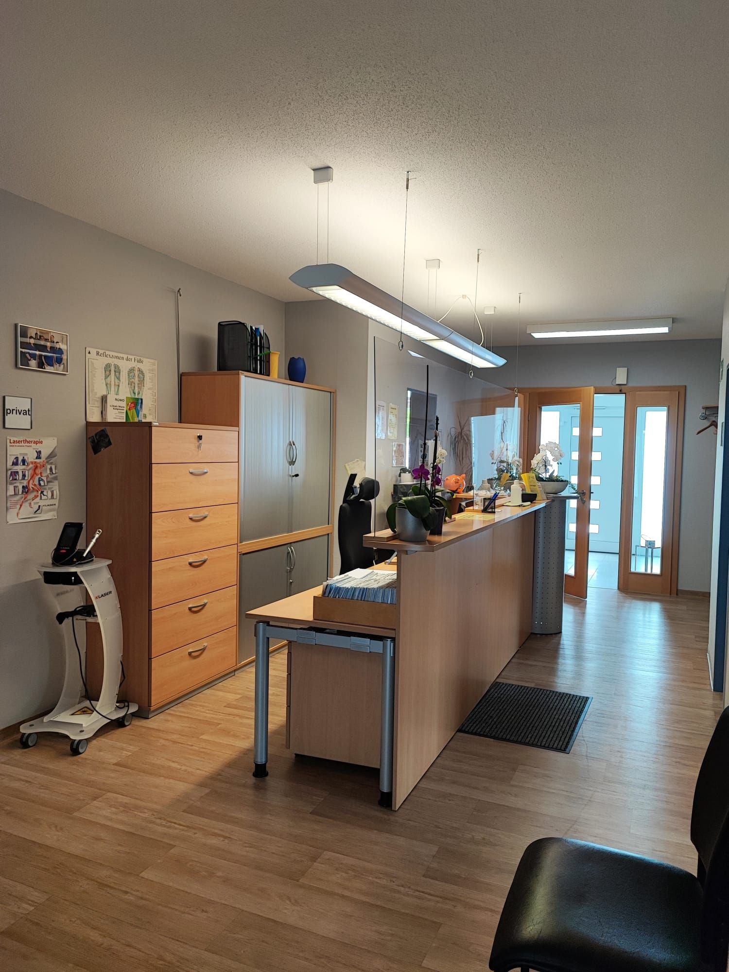 Empfangsbereich mit Schreibtisch, Schränken, Wartebereich und Doppeltüren.