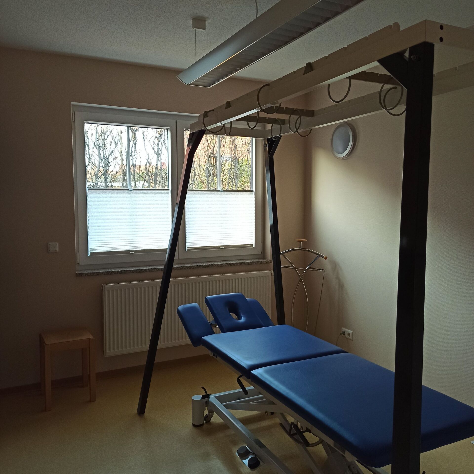 Ein Therapieraum mit Behandlungstisch, Hängevorrichtung und Fenster.