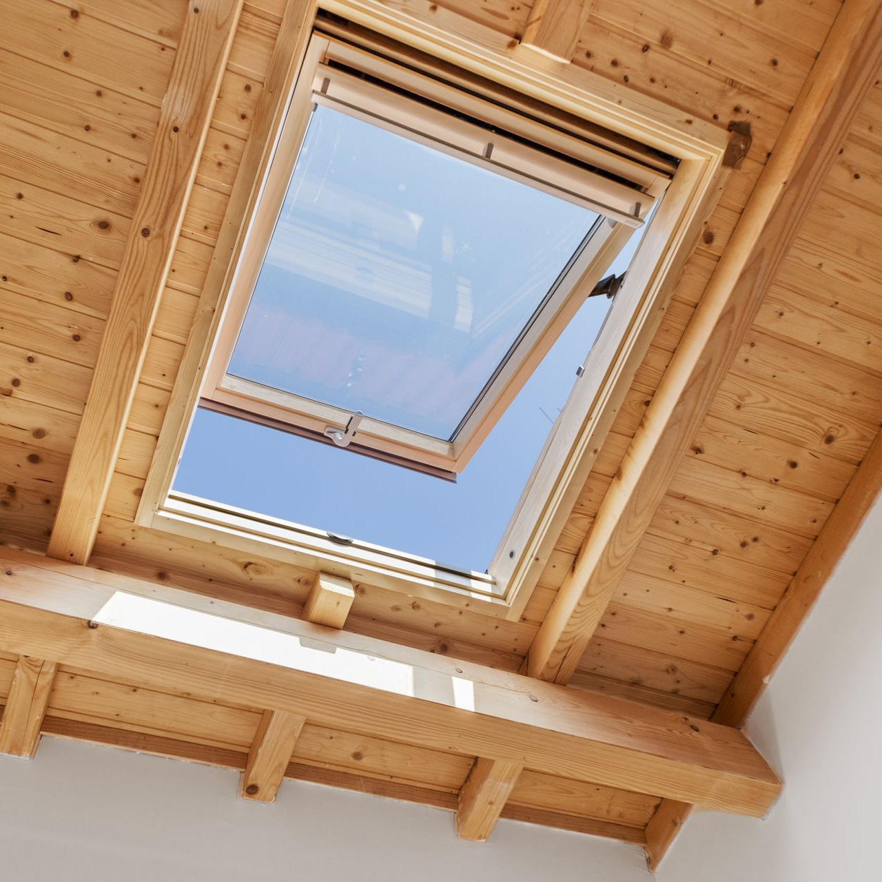 Puits de lumière ouvert dans le plafond en bois, ciel bleu éclatant visible.