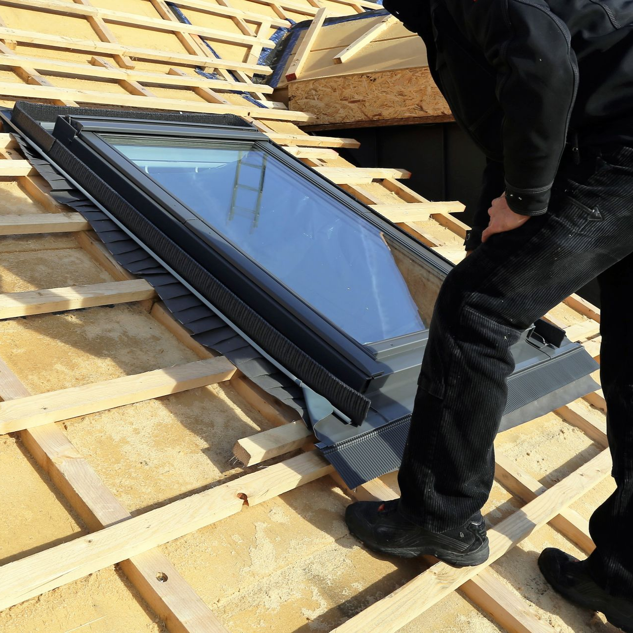 Personne installant un puits de lumière sur un toit en bois.