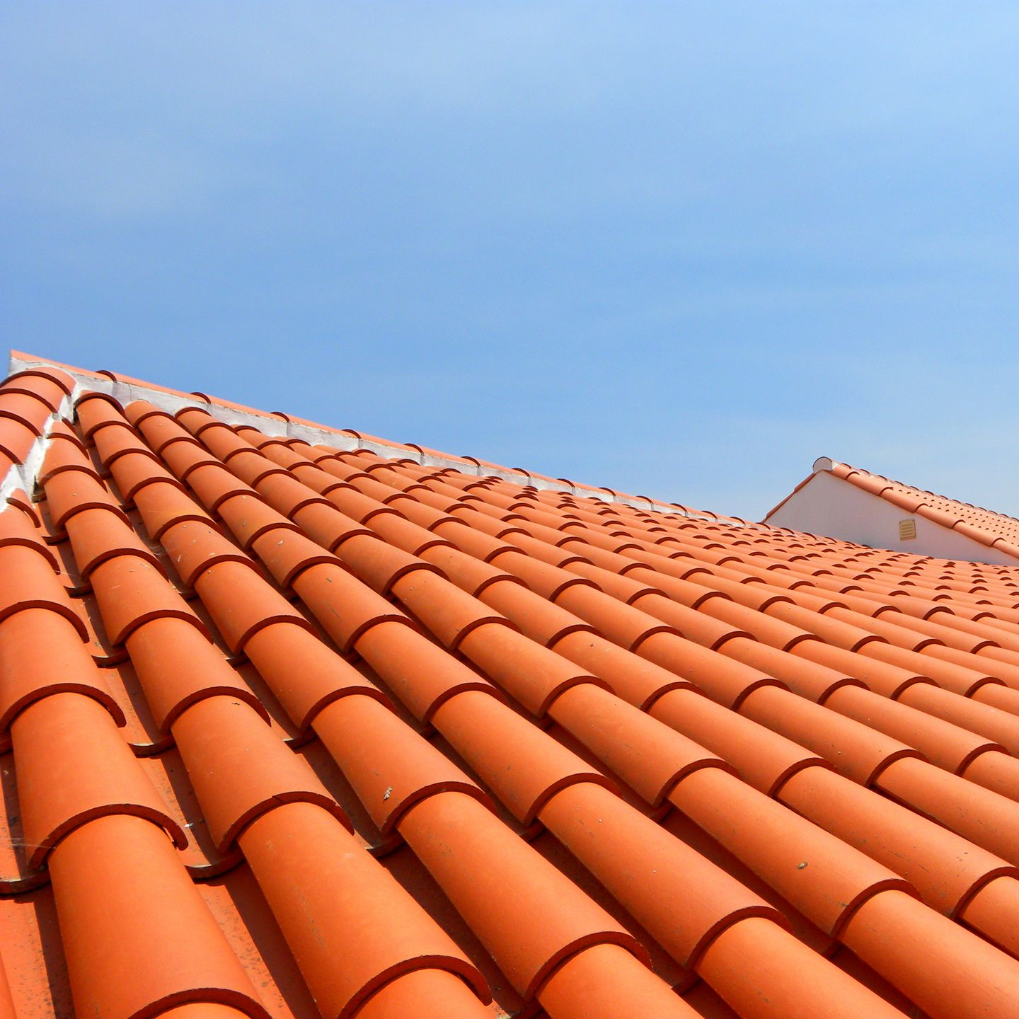 Des tuiles rouges en terre cuite se détachant sur un ciel bleu limpide.