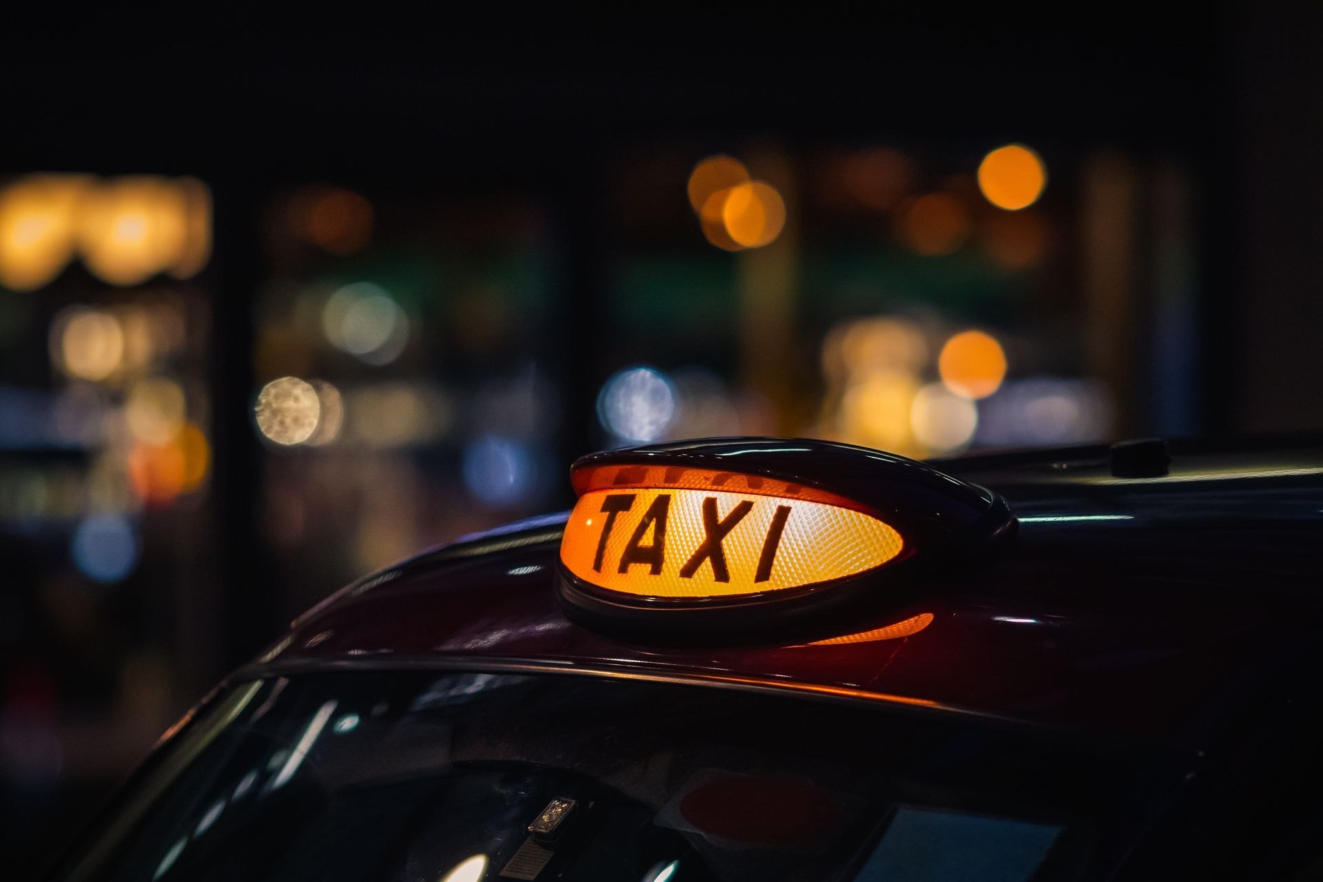 Panneau TAXI orange lumineux sur le toit d'une voiture, la nuit, avec les lumières de la ville floues en arrière-plan.