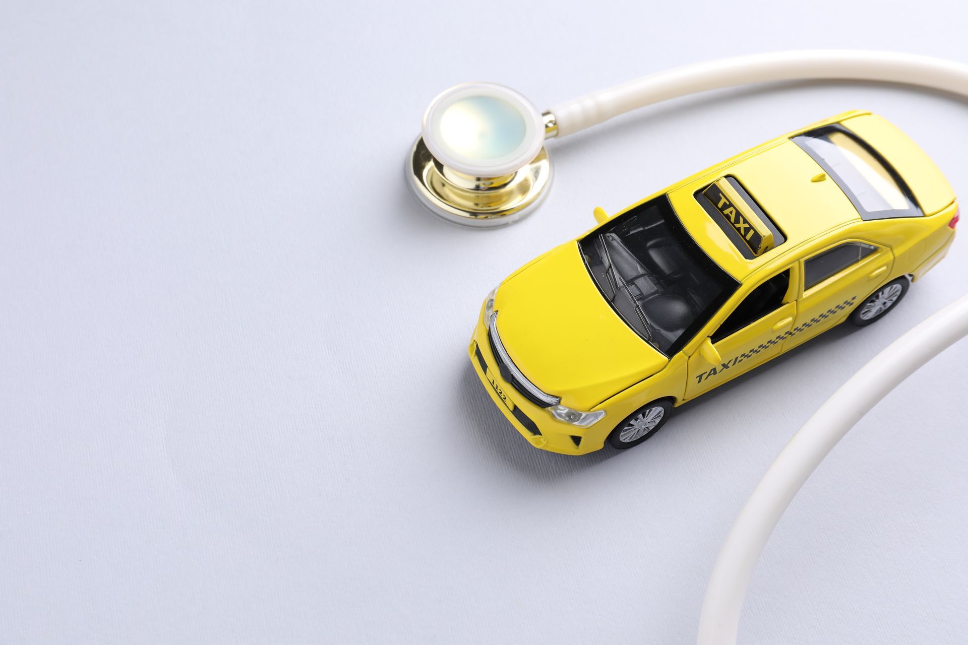 Un taxi miniature jaune à côté d'un stéthoscope blanc sur fond clair.
