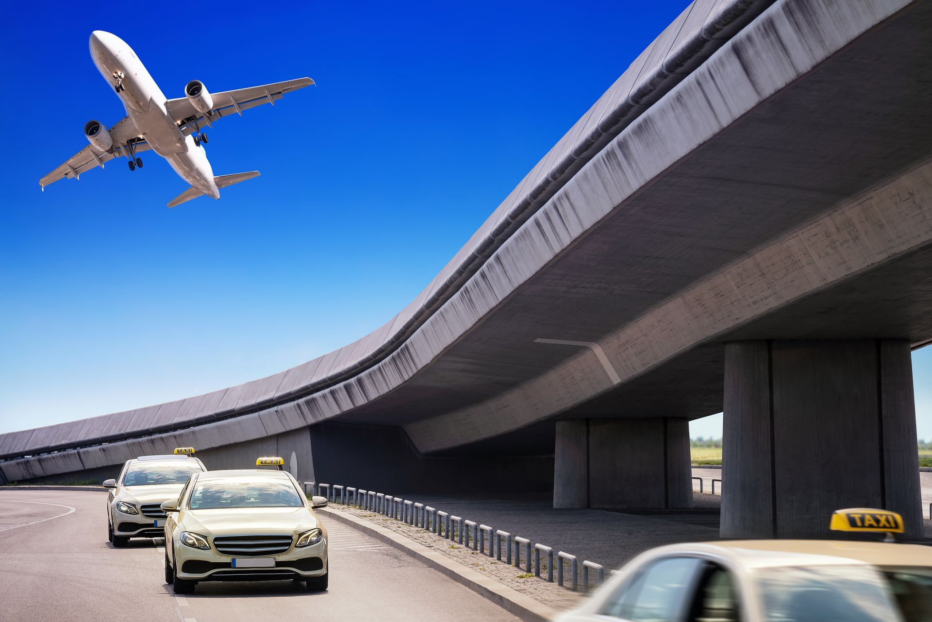 Des voitures circulent sous un pont tandis qu'un avion survole la zone dans un ciel bleu.