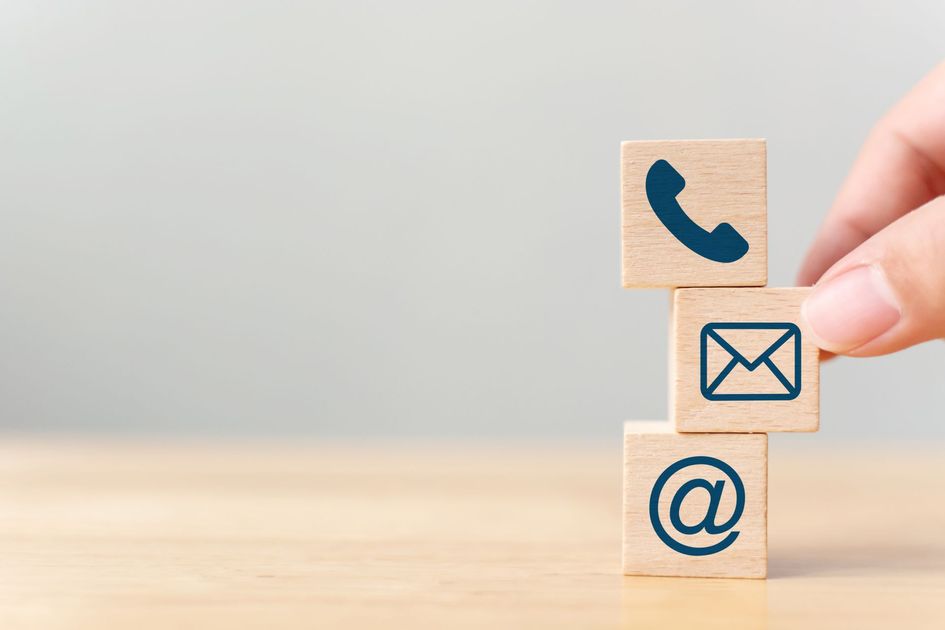 Pose manuelle de blocs de bois empilés avec des icônes de téléphone, d'e-mail et de symbole @ sur une table.