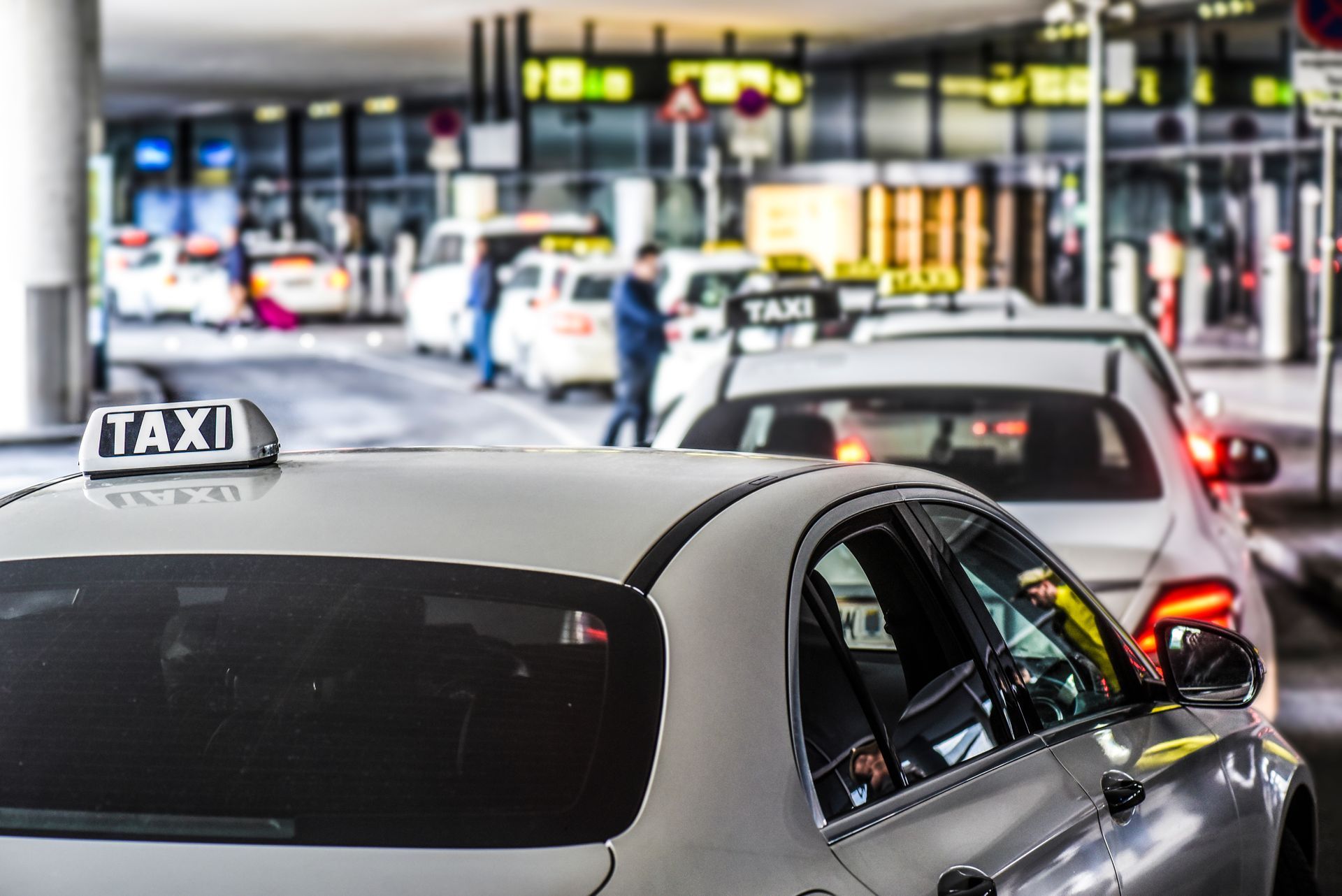 File d'attente de taxis au bord du trottoir de l'aéroport, plusieurs voitures attendant.