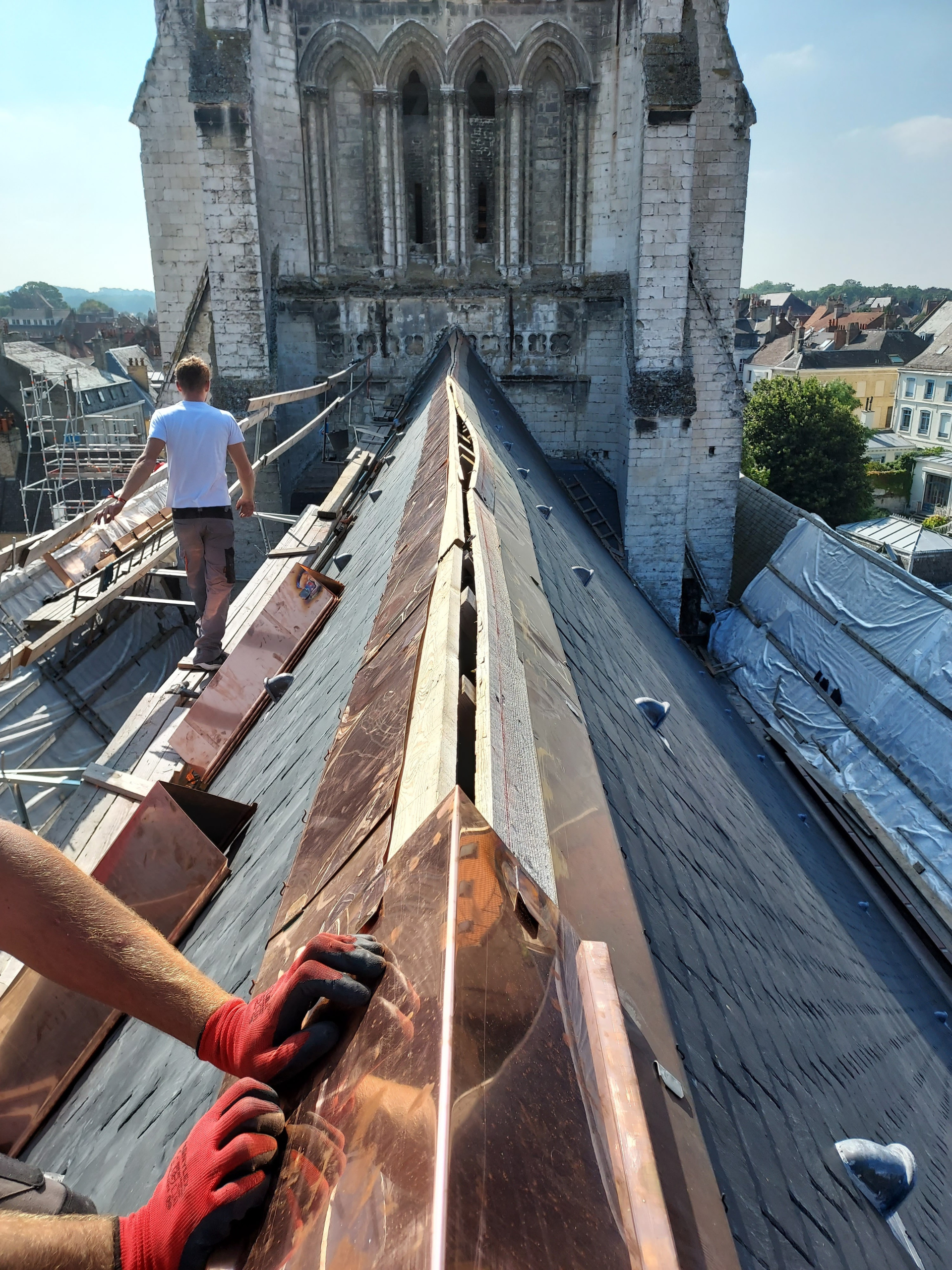Des ouvriers installent une toiture en cuivre sur la flèche d'une cathédrale, par une journée ensoleillée.