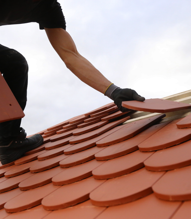 Personne installant des tuiles rouges sur une structure de toit en bois.