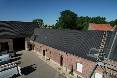 Bâtiment en briques avec toit en tuiles noires, deux puits de lumière, une échelle et un ciel bleu.