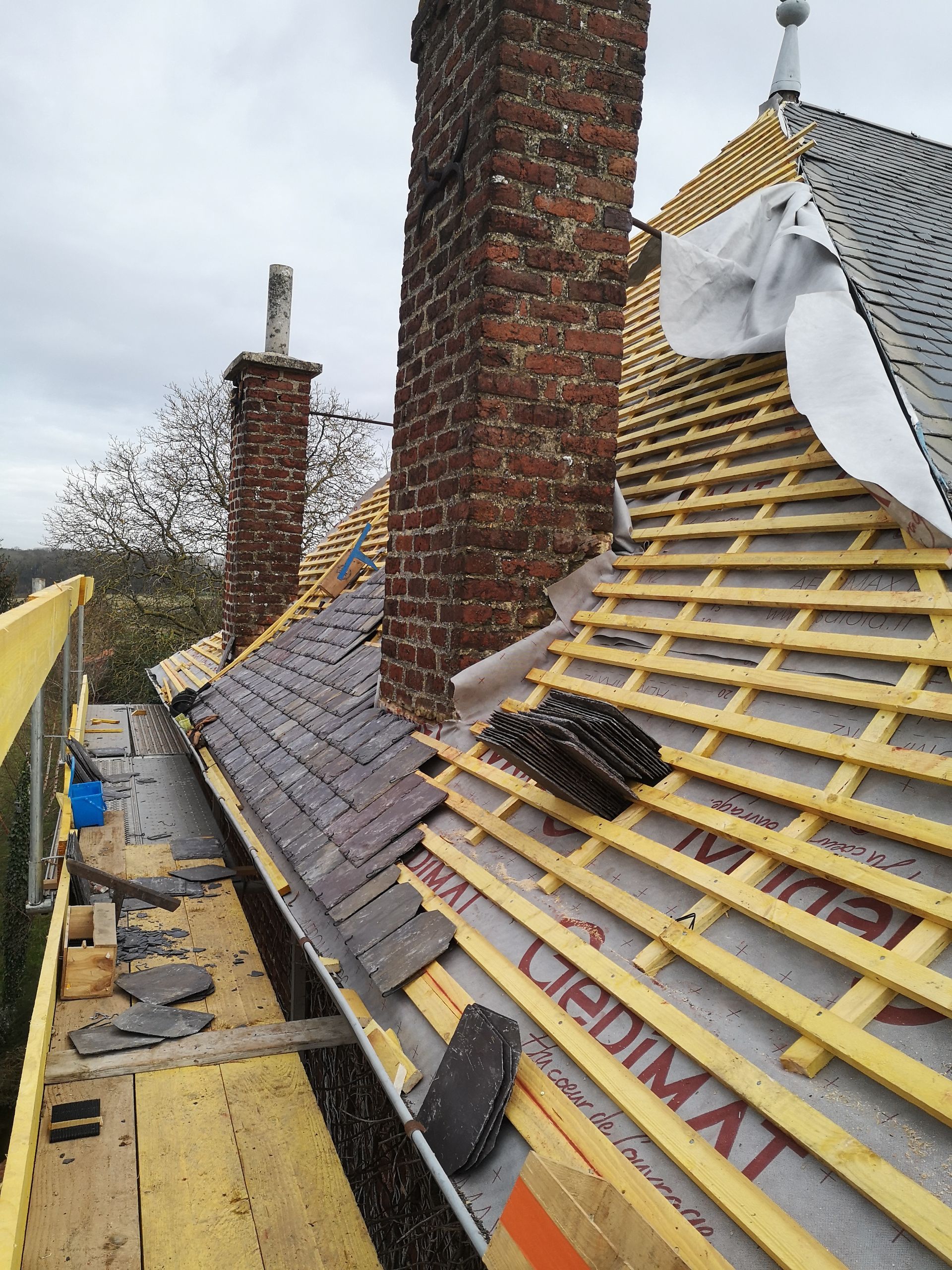 Toiture en construction avec chevrons apparents, cheminées en briques et couverture partielle en ardoise.