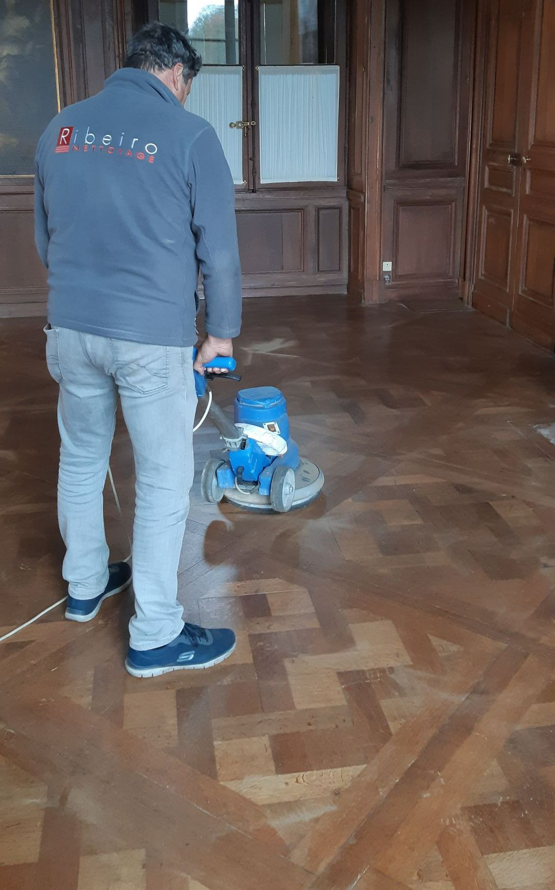 Un homme nettoie un sol en bois avec une monobrosse