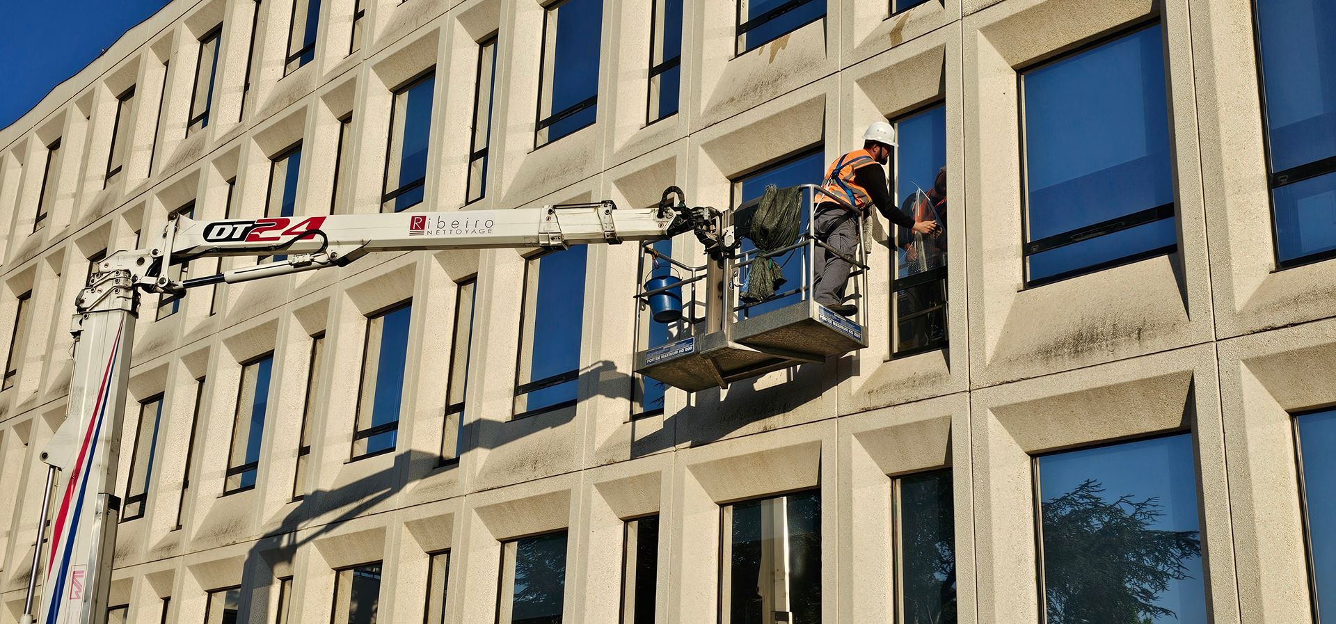 Un homme sur une nacelle devant un bâtiment vitré