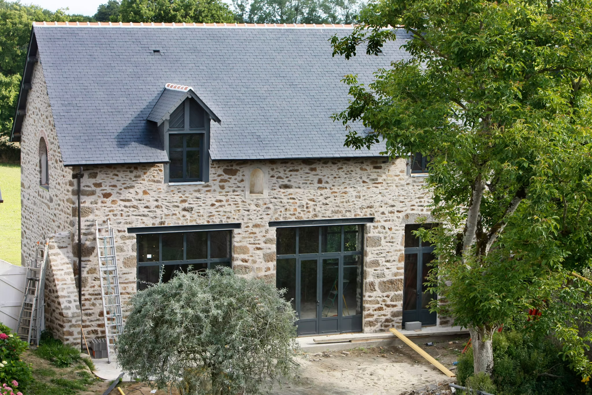 Une maison en pierre avec un toit en ardoise, de grandes fenêtres et une lucarne.