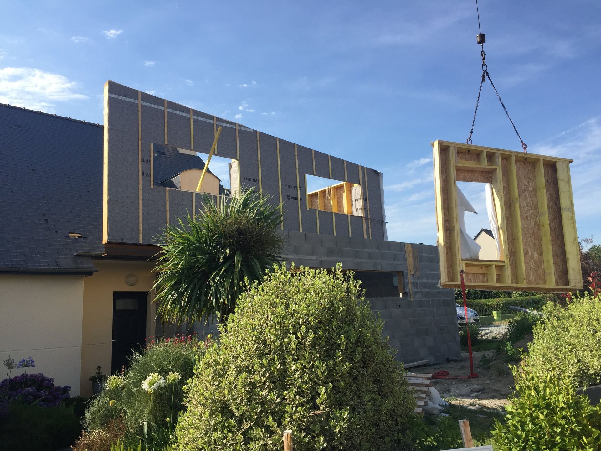 Une grue soulève un panneau destiné à créer une ossature bois.
