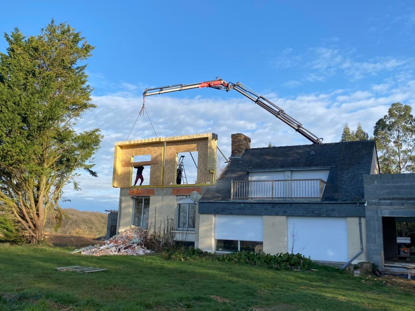 Une grue installe un mur à ossature bois sur le premier étage d'une maison.