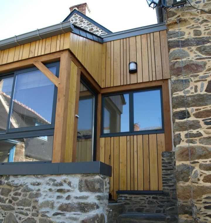Une extension en bois, avec un bardage vertical, de grandes fenêtres et des murs en pierre.