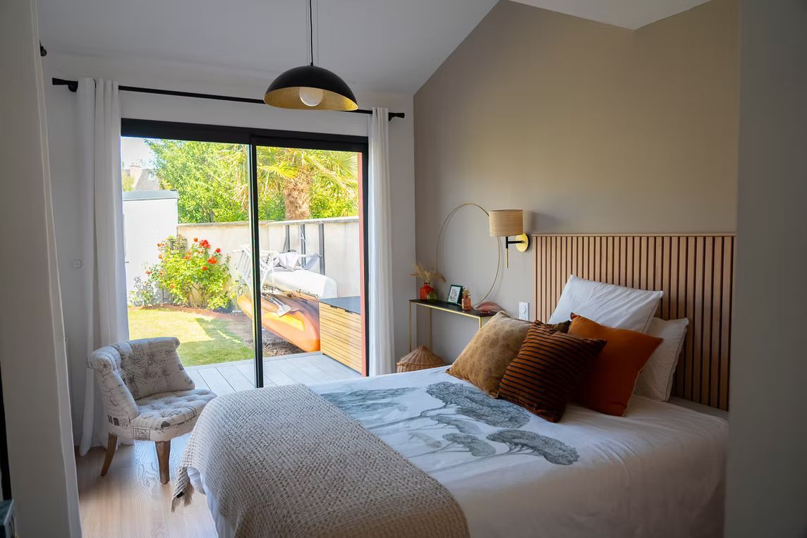 Une chambre avec un lit, une tête de lit à lattes de bois et des portes coulissantes donnant sur un jardin.