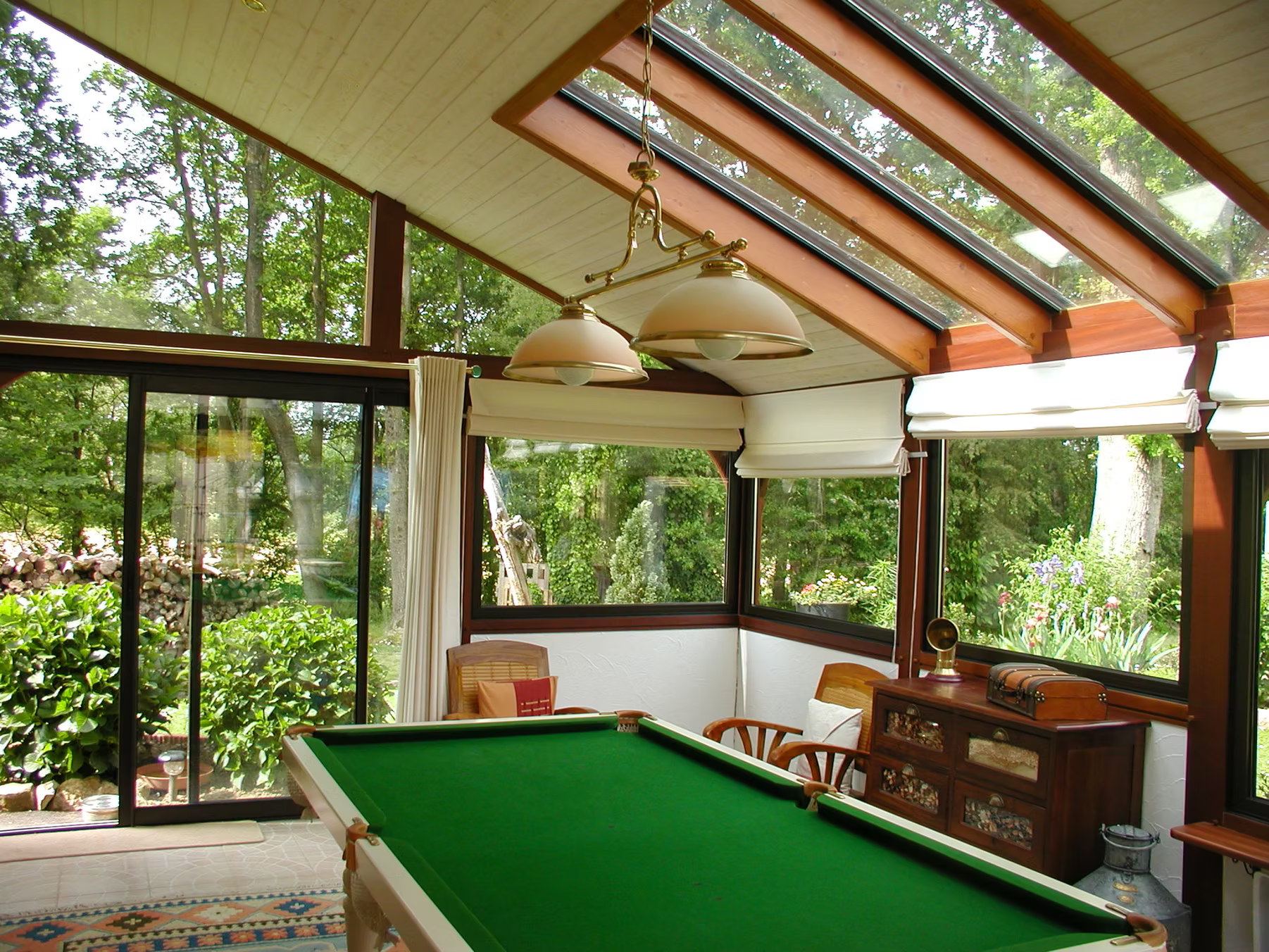 Table de billard dans une véranda avec plafond en verre, donnant sur un extérieur verdoyant et luxuriant.