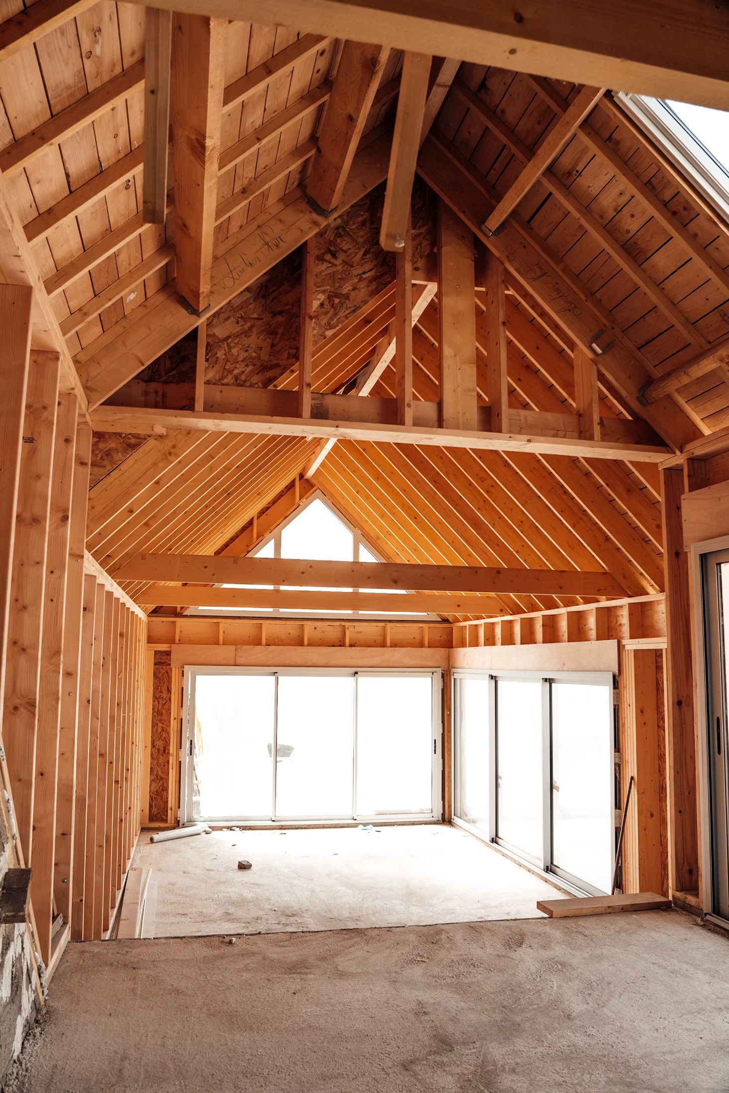 Intérieur d'une pièce avec poutres en bois apparentes, charpente et grandes fenêtres.