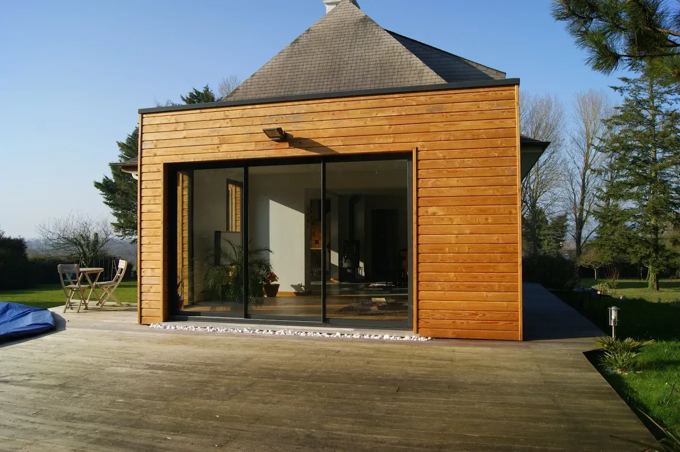 Extension moderne avec un bardage bois et grandes portes vitrées.