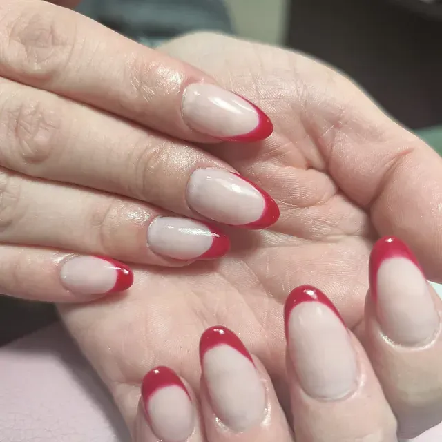 Un primer plano de la mano de una mujer con uñas rojas y blancas.