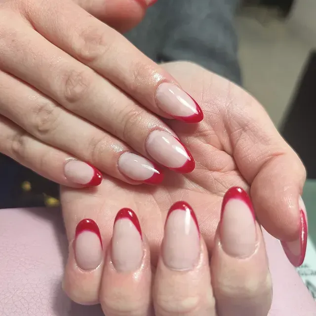 Un primer plano de las uñas de una mujer con una manicura francesa roja.