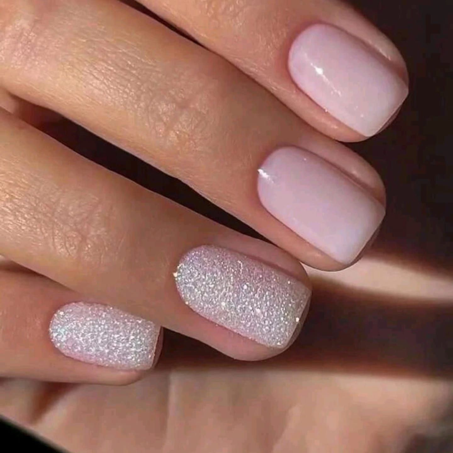 Un primer plano de las uñas de una mujer con esmalte de uñas rosa y blanco.
