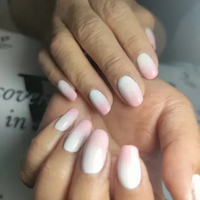 Un primer plano de las manos de una mujer con uñas rosas y blancas.