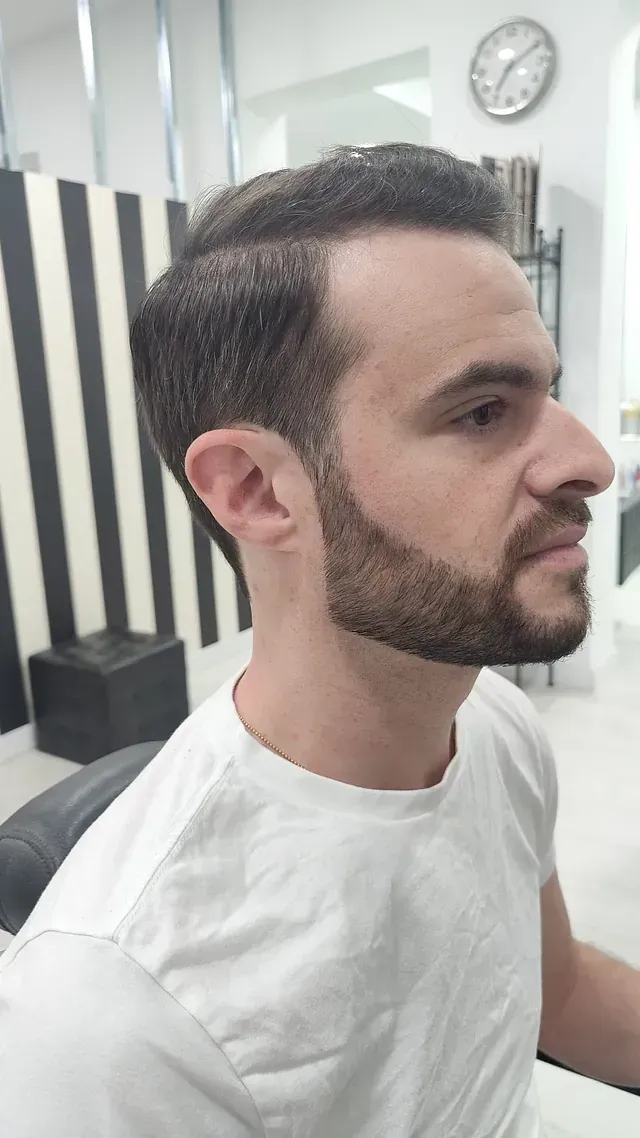 Un hombre con barba y camisa blanca está sentado en una silla.