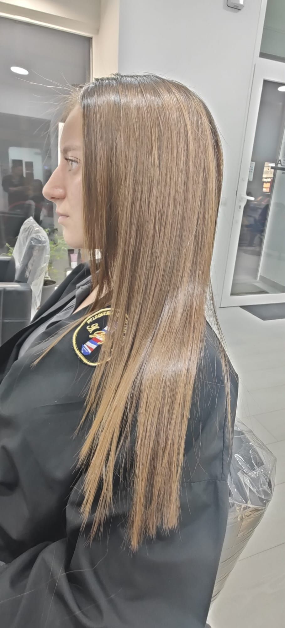 Una mujer con cabello largo está sentada en una silla en una peluquería.