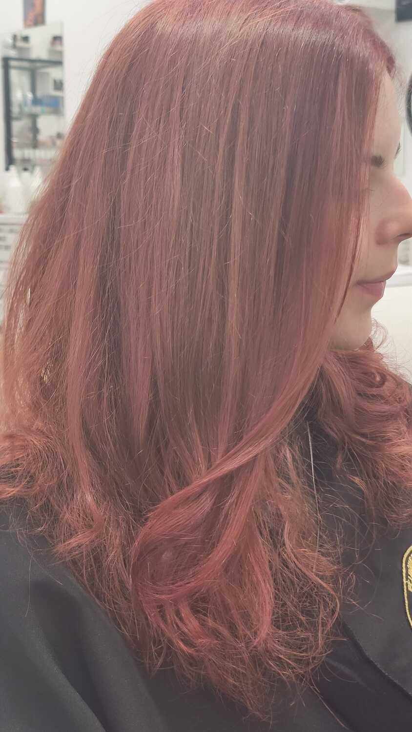 Una mujer con cabello largo y rojo está sentada en una silla en una peluquería.